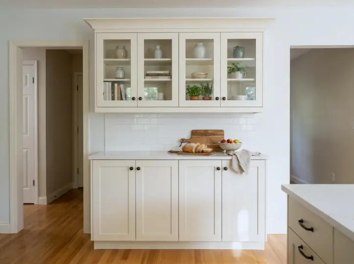 White glass-front upper display cabinets over shaker lowers with a marble counter and vintage stoneware