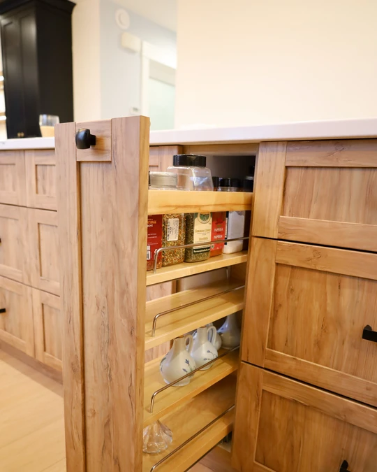 Warm oak pull-out pantry cabinet with narrow tiered shelves holding spices, oils and pantry staples