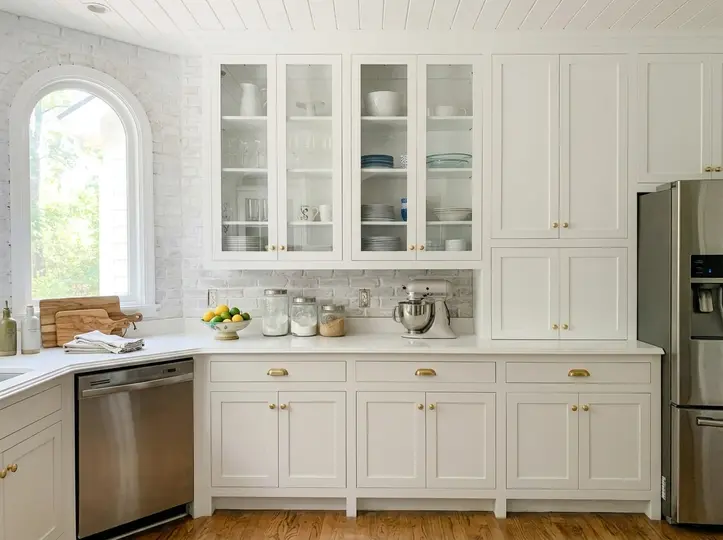 White inset shaker kitchen with glass-front uppers, an arched window, marble counter and stainless dishwasher